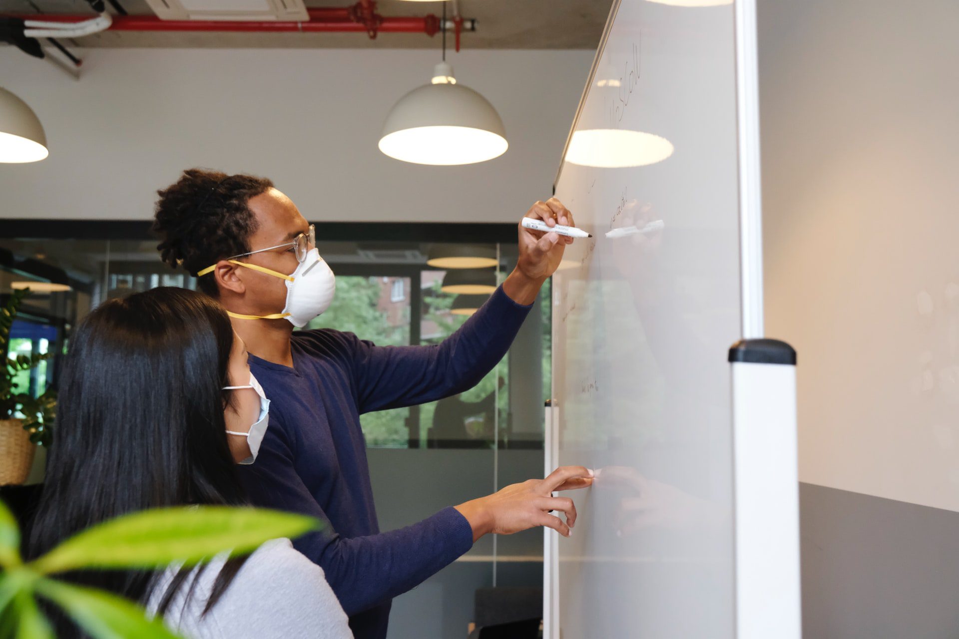 A woman and man work together at a white board, both with Covid-19 masks on.