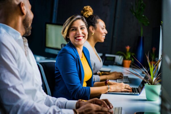 Woman in blue suit jacket smiles at her colleague while working on their laptops