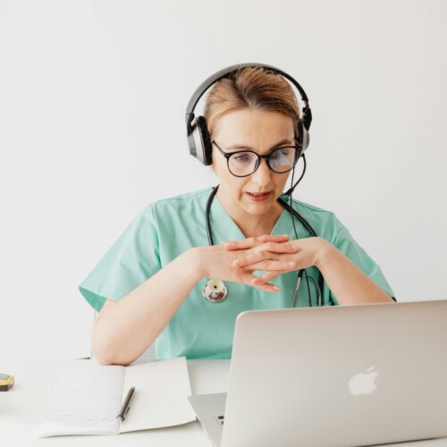 Woman in scrubs sitting in front of a laptop on a video call