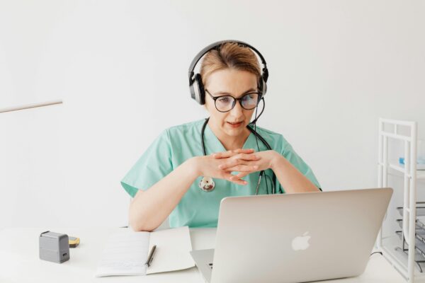 Woman in scrubs sitting in front of a laptop on a video call