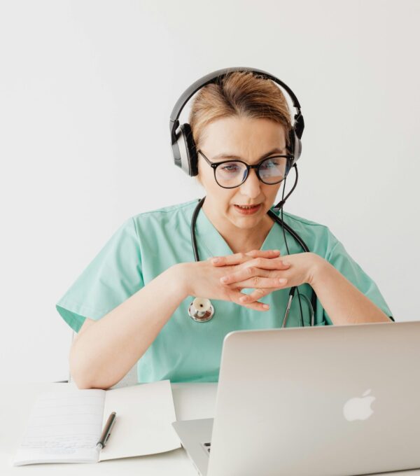 Woman in scrubs sitting in front of a laptop on a video call