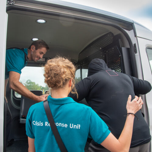 A man and woman in Crisis Response Unit t-shirts help a person into a van.