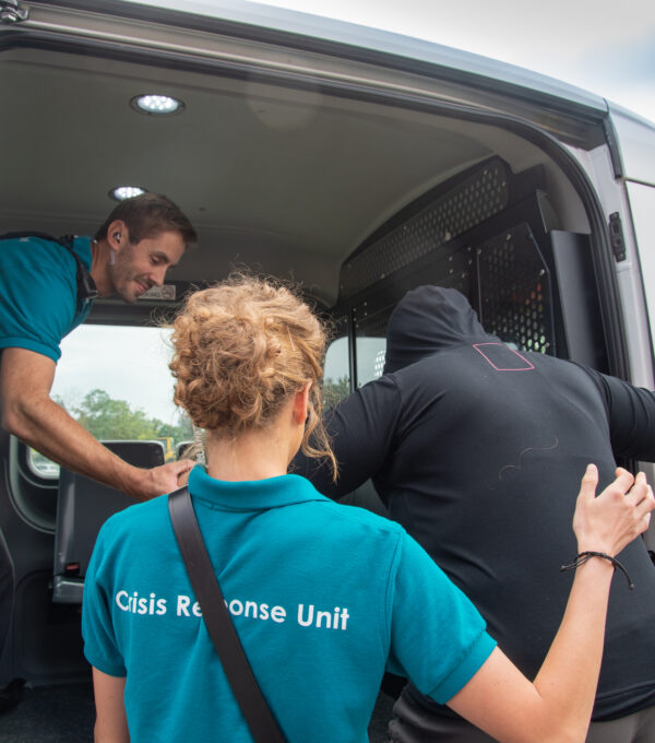 A man and woman in Crisis Response Unit t-shirts help a person into a van.