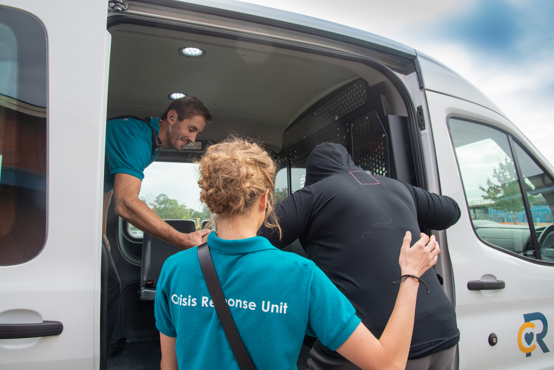 A man and woman in Crisis Response Unit t-shirts help a person into a van.