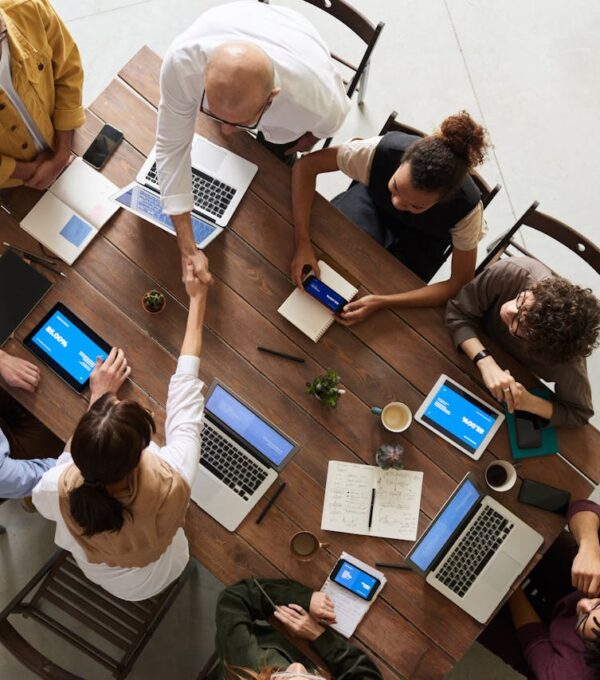 Eight people sitting around a table with laptops, notebooks, and phones. Two people are shaking hands.