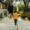 Back of person in yellow t shirt, jeans, and white shoes walking down a neighborhood alley.