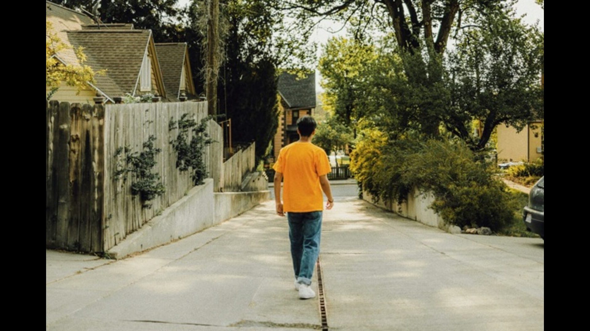 Back of person in yellow t shirt, jeans, and white shoes walking down a neighborhood alley.
