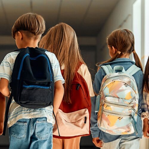 Backside of elementary-aged kids walking in school with backpacks.