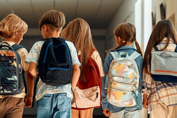 Backside of elementary-aged kids walking in school with backpacks.
