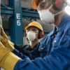 Two people working in factory with goggles and masks.