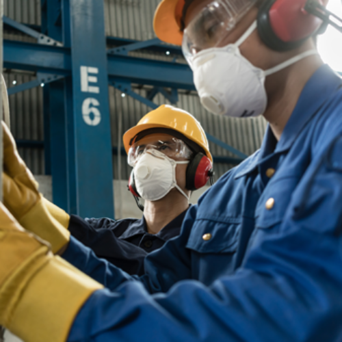 Two people working in factory with goggles and masks.